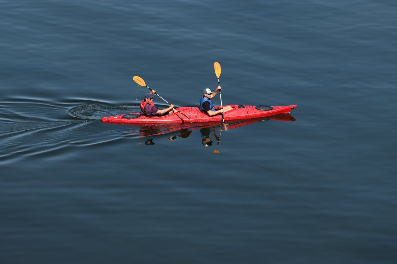 Two people kayaking in a red kayak on a serene lake in Sweden. Outdoor recreation and adventure.